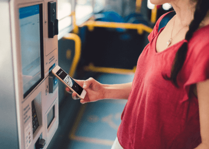 a lady holding a cell phone and standing in front of a bus ticket machine